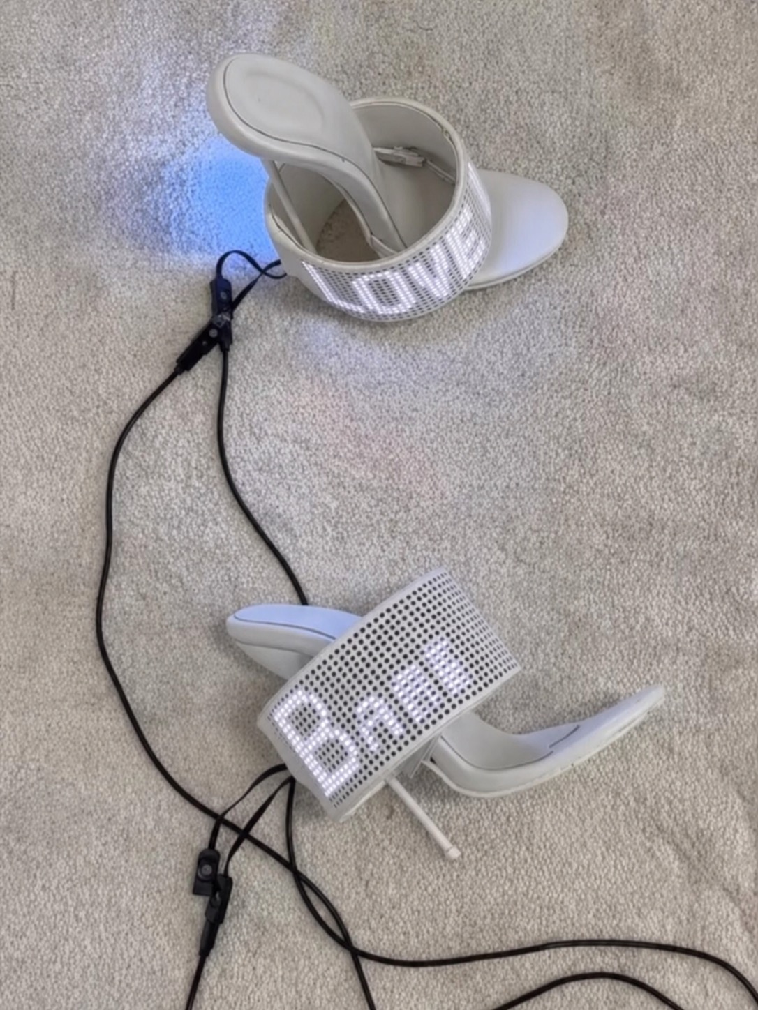 A pair of white LED shoes on carpet with text glowing across the straps.