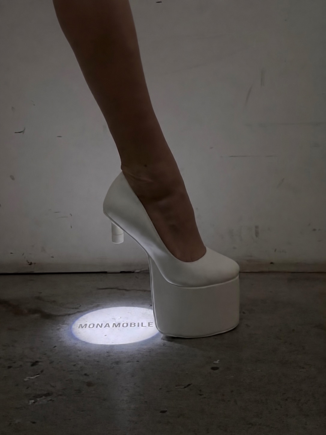A white platform heel projecting Monamobile text on the floor.