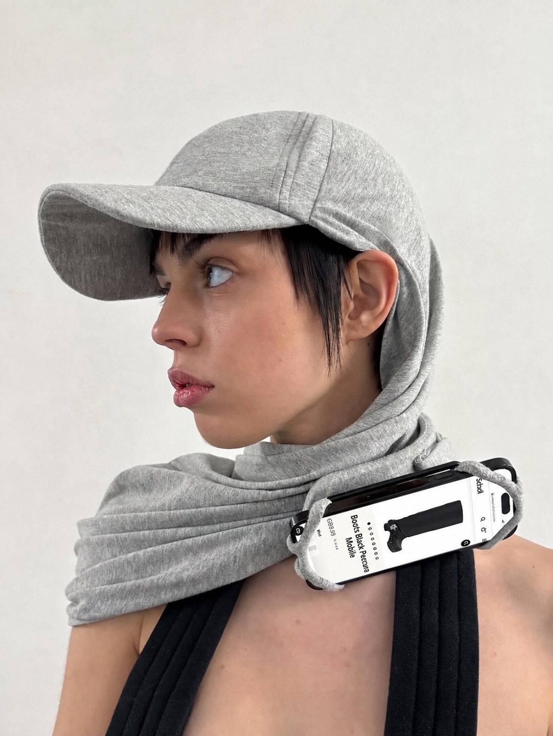 A grey hooded look with a white tech object strapped across the shoulder and neck.