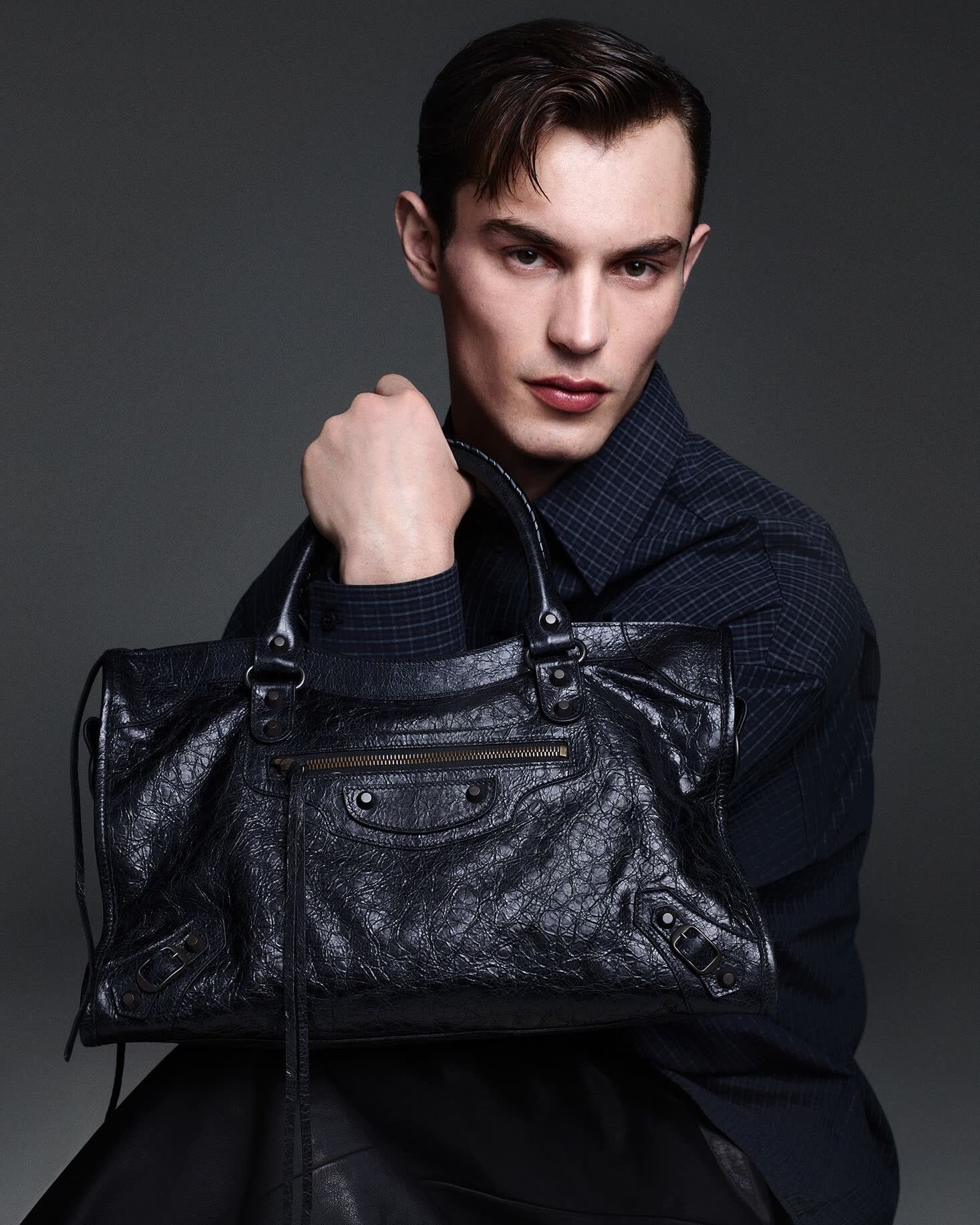 A male model holding a black Balenciaga Le City bag