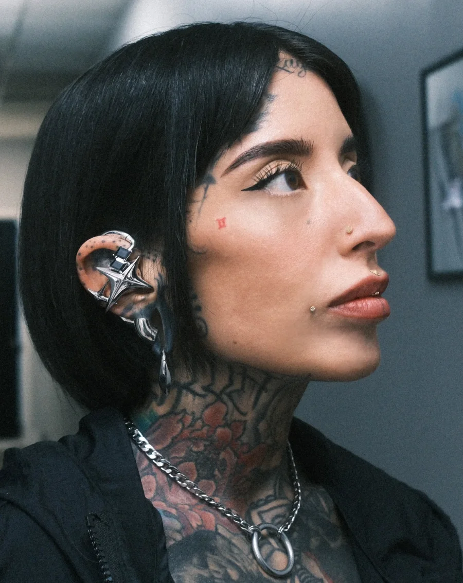 Black-haired wearer with tattoos and layered silver jewelry wearing NEBULA earphones